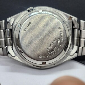 May include: Close-up of the back of a silver-toned Seiko watch. The watch has a stainless steel back with the brand name and model information. The watch band is also silver-toned and made of metal.