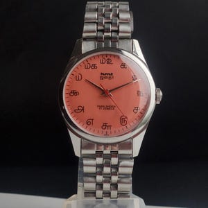 Puede incluir: Un reloj de pulsera plateado con una esfera de color salm&oacute;n y una correa plateada a juego. La esfera del reloj presenta s&iacute;mbolos &uacute;nicos y el texto "PARA SHOCK 17 JEWELS". El reloj tiene un dise&ntilde;o cl&aacute;sico.