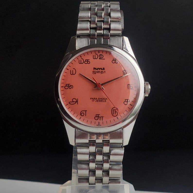 Puede incluir: Un reloj de pulsera plateado con una esfera de color salm&oacute;n y una correa plateada a juego. La esfera del reloj presenta s&iacute;mbolos &uacute;nicos y el texto "PARA SHOCK 17 JEWELS". El reloj tiene un dise&ntilde;o cl&aacute;sico.