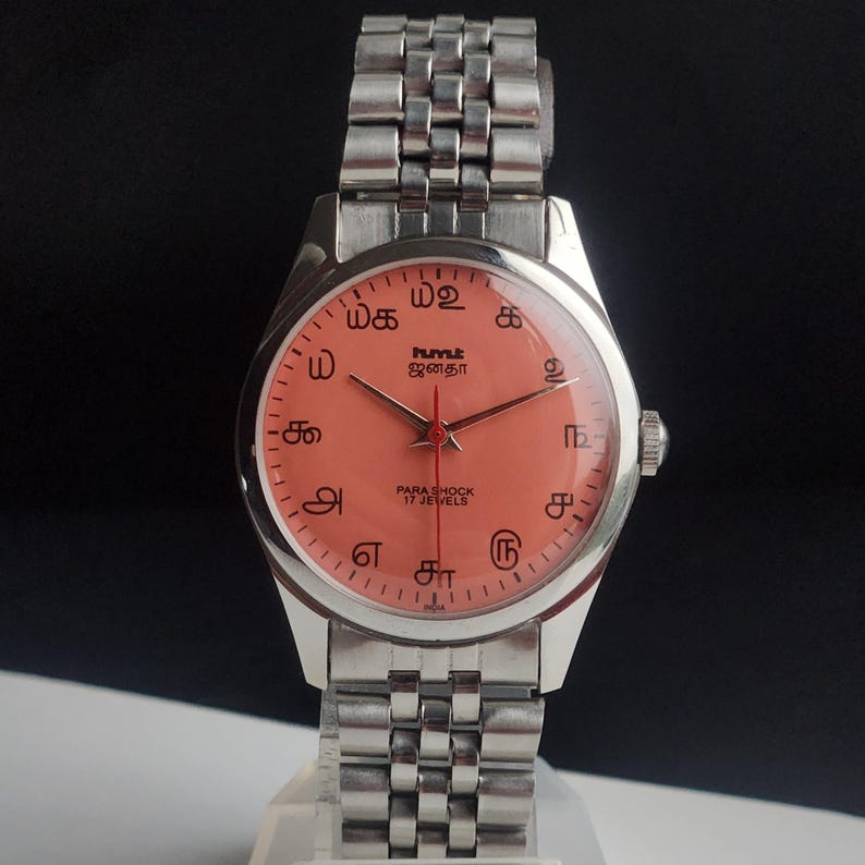Puede incluir: Un reloj de pulsera vintage con una correa y caja de metal plateado. La esfera del reloj es de color salm&oacute;n con marcas y agujas negras. La esfera tiene texto en idioma extranjero y las palabras "PARA SHOCK 17 JEWELS".