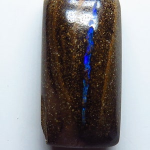 Puede incluir: Un cabujón de ópalo rectangular de color marrón oscuro y azul. El ópalo tiene un destello de color azul.