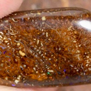 Könnte beinhalten: Ein brauner und weißer Opal-Cabochon mit einer glatten, polierten Oberfläche. Der Stein hat ein einzigartiges Muster aus Wirbeln und Einschlüssen.