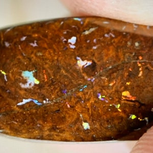 May include: A brown opal cabochon with iridescent flashes of blue, green, and yellow. The opal has a rough, natural texture.