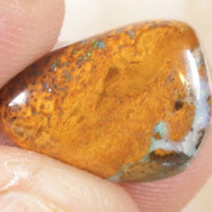 May include: A smooth, polished, orange opal gemstone with a white and green iridescent sheen.