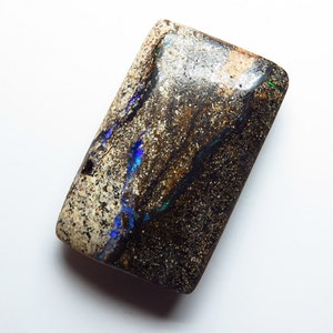 May include: A dark brown, black, and white opal cabochon with blue and green flashes of color.