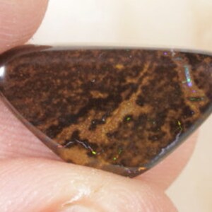 May include: A brown and black opal cabochon with iridescent flashes of color. The opal is cut in a triangular shape and has a smooth, polished surface.