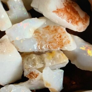 Könnte beinhalten: Eine Sammlung von weißen Opal-Rohsteinen, einige mit einem Hauch von irisierenden Farben. Die Steine sind in verschiedenen Formen und Größen.
