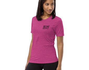 May include: A magenta short-sleeve t-shirt with the embroidered text "RN Registered Nurse" in black. The shirt is made of a soft, textured fabric and is worn by a person.