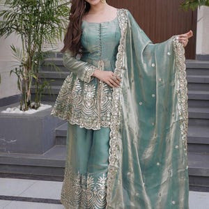 Peut inclure: Une tenue de cérémonie vert d'eau avec des broderies dorées. L'ensemble comprend un haut à manches longues et un pantalon palazzo assorti, complété par une écharpe transparente avec des bordures dorées. Des boucles d'oreilles dorées complètent la tenue.