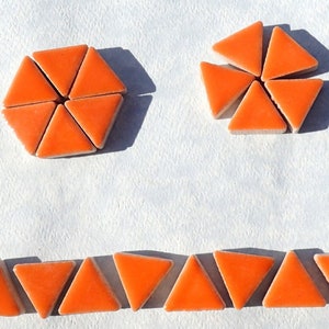 May include: Orange triangular ceramic tiles arranged in a hexagonal and circular pattern. The tiles are on a white surface.