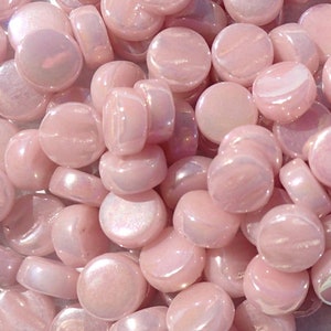 May include: A pile of iridescent pink glass beads, each bead is round and flat with a smooth surface.