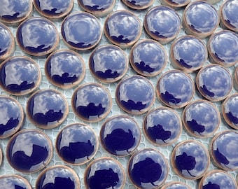 May include: Close-up of a mosaic tile pattern. The tiles are a deep blue color with a glossy finish, arranged in a grid. The tiles reflect the sky and clouds. The grout lines are a light gray color.