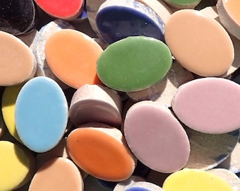 May include: A collection of colorful, oval-shaped mosaic tiles in various shades including black, red, orange, yellow, green, blue, and pink. The tiles are arranged on a surface of smaller, irregular pieces.