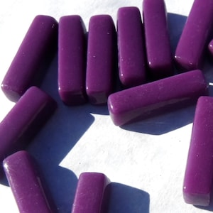 May include: A scattering of glossy, rectangular, purple beads. The beads have rounded edges and are spread across a white surface. The beads are a deep, rich shade of purple, and appear to be made of glass or a similar material.