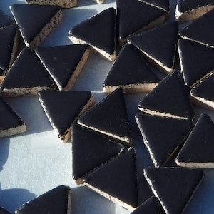 May include: A collection of small, triangular tiles with a glossy black surface and a beige, textured edge. The tiles are arranged in a scattered pattern, suitable for mosaic projects or decorative applications.