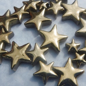 May include: A collection of gold-colored star-shaped decorative objects. The stars vary in size and are arranged in a circular pattern. The metallic finish reflects light, creating a shiny appearance. These decorative stars could be used for crafts or home decor.