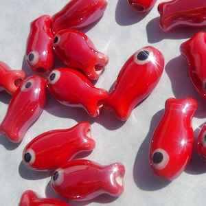 May include: A collection of red ceramic fish beads with black eyes. The beads are glossy and have a slightly irregular shape.