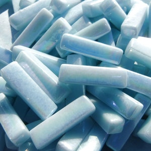 May include: A pile of light blue iridescent glass tiles in a rectangular shape. The tiles are smooth and have a subtle sparkle.