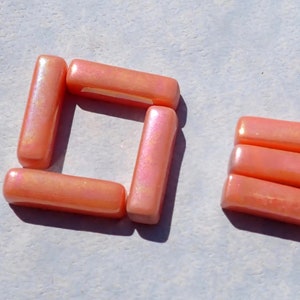 May include: A set of iridescent pink glass tiles in two different shapes. The first shape is a square made of four tiles, and the second shape is a stack of three tiles.