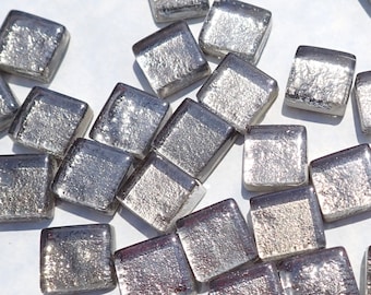 May include: A collection of silver-colored glass tiles with a textured surface. The tiles are square shaped and have a slightly iridescent sheen.