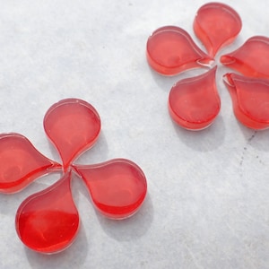 May include: Two red glass flower shapes with five petals each. The petals are teardrop shaped.