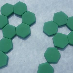 May include: Green, hexagonal tiles arranged in floral patterns. The tiles are a solid, matte green color and are arranged in a symmetrical design against a light blue background. The tiles are likely for crafts or home decor.