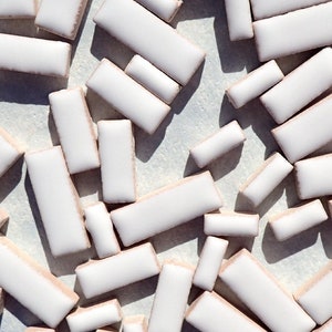 May include: A collection of white rectangular tiles with rounded edges are scattered across a light surface. Each tile has a subtle beige border. The image suggests materials for a craft project, possibly mosaic tiles, arranged randomly.