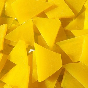 May include: A close-up shot of numerous yellow, irregularly shaped glass pieces. The pieces are mostly triangular, with some having a more geometric form. The glass has a translucent quality, and the overall effect is bright and sunny.