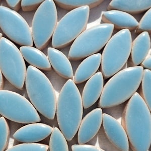 May include: Close-up of a mosaic tile design featuring numerous light blue, leaf-shaped tiles. The tiles are arranged closely together, creating a textured surface. The tiles have a glossy finish and are set against a neutral background.
