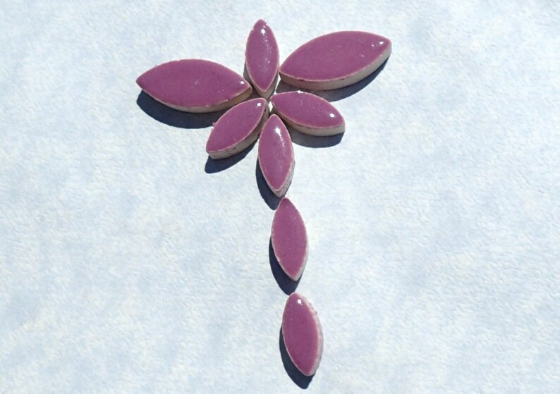 Pode incluir: Um desenho de mosaico de azulejos em forma de flor roxa, feito de pequenos azulejos ovais. Os azulejos est&atilde;o dispostos em forma de flor com um caule.