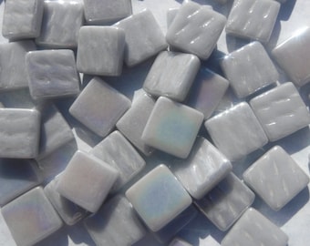 May include: A collection of small, square, iridescent glass tiles in a light gray color. The tiles have a textured surface and are perfect for crafting projects.