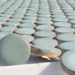 May include: A close-up of a collection of light blue round ceramic tiles. The tiles are arranged in a staggered pattern, creating a textured surface.