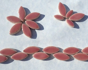 May include: A set of pink ceramic tiles in the shape of elongated ovals. The tiles are arranged in a flower pattern and a straight line.