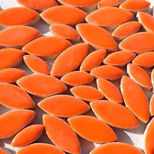 May include: A collection of orange ceramic tiles shaped like elongated leaves. The tiles are glossy and have a smooth surface.