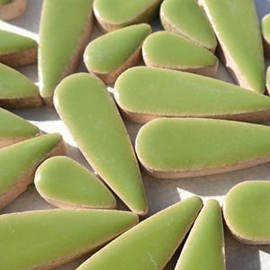 May include: A collection of green ceramic tile pieces in various sizes and shapes, resembling leaves or teardrops. The tiles have a smooth, glossy finish and a slightly irregular edge.