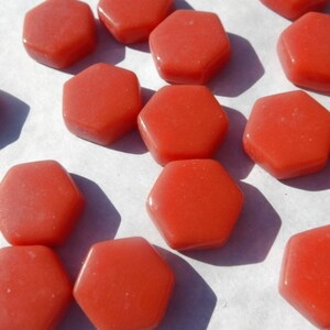 May include: A collection of 14 coral-colored hexagonal glass tiles. The tiles are smooth and have a slightly textured surface.