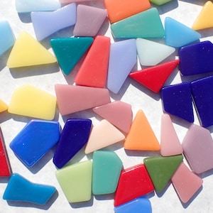 May include: A collection of colorful glass mosaic tiles in various shapes and sizes. The tiles are arranged in a random pattern on a white surface.
