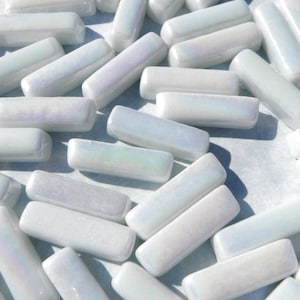 May include: A collection of white iridescent glass tiles in a rectangular shape. The tiles are scattered on a white surface.