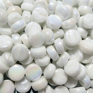 May include: A pile of white iridescent glass pebbles. The pebbles are round and smooth, with a slight shimmer.
