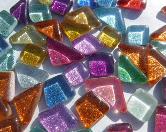May include: Assortment of colourful, glittery glass tiles in various shapes, including squares and triangles. The tiles have an iridescent finish and are perfect for crafting projects.