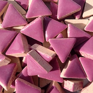 May include: A pile of small, triangular ceramic tiles in a deep pink colour. The tiles have a glossy finish and are arranged in a random pattern.
