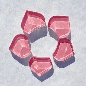 May include: Five pink glass flower petals with a white swirl pattern, arranged in a circle.