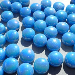 Puede incluir: Primer plano de numerosas canicas de vidrio azul iridiscente. Cada canica tiene una superficie brillante y reflectante, creando un efecto brillante. Las canicas est&aacute;n dispersas, lo que sugiere un juego o un art&iacute;culo decorativo. Cada canica mide aproximadamente 2,5 cm de di&aacute;metro.