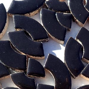 May include: A collection of glossy, black, curved mosaic tiles with a light beige, textured edge. The tiles are arranged in a scattered pattern, creating a visually interesting texture. Ideal for craft projects.