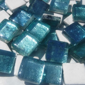 May include: A collection of square glass mosaic tiles in shades of teal, turquoise, and deep blue, interspersed with white tiles. The tiles have a glossy, reflective surface, ideal for craft projects.