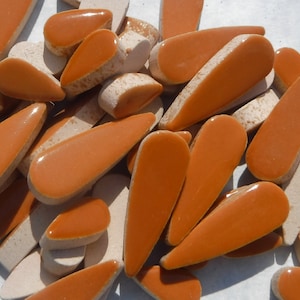 May include: A collection of terracotta-colored ceramic tiles in a teardrop shape. The tiles are glazed and have a smooth, glossy finish.