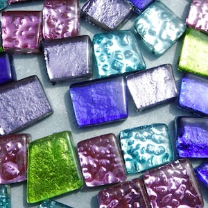 May include: A collection of colourful, square glass tiles in shades of blue, purple, green, and teal. Some tiles have a textured surface, while others are smooth. The tiles are arranged closely together, creating a mosaic effect.