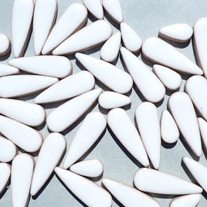 May include: A collection of white ceramic teardrop-shaped tiles. The tiles are arranged in a random pattern and are all the same size and shape.