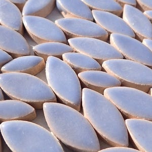 May include: Close-up of a collection of light blue, oval-shaped ceramic tiles. Each tile has a smooth, glossy surface and a light brown, textured edge. The tiles are arranged in a pattern, creating a visually appealing texture.