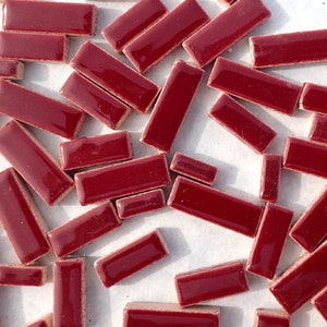 May include: A collection of small, rectangular, glossy, burgundy-colored tiles. The tiles are scattered across a light-colored surface, showcasing their smooth, reflective finish. These decorative tiles are suitable for various craft and home improvement projects.